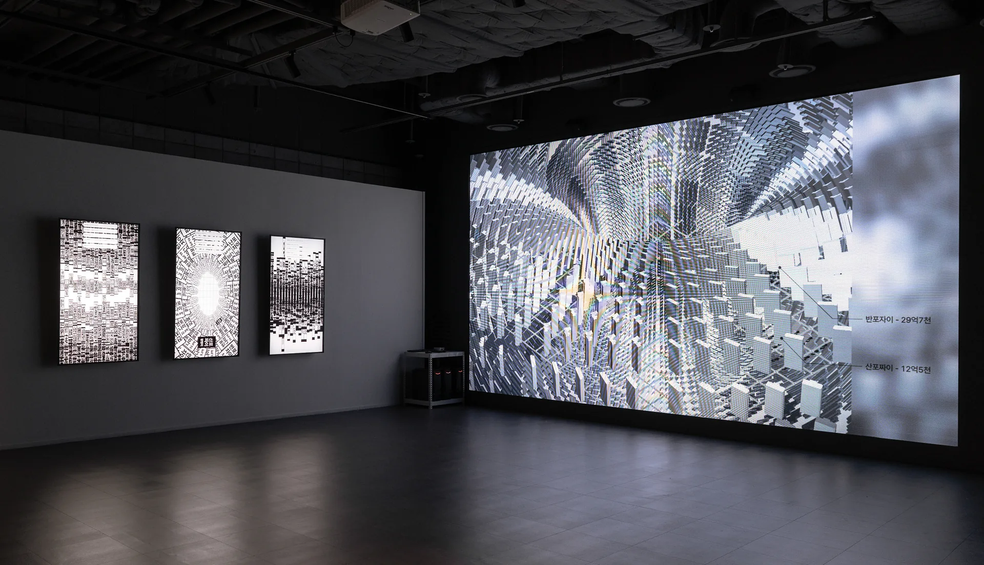 Wide installation view of Banpo-Xism with three vertical screens and a white geometric apartment field. Artwork by Jeanyoon Choi.
