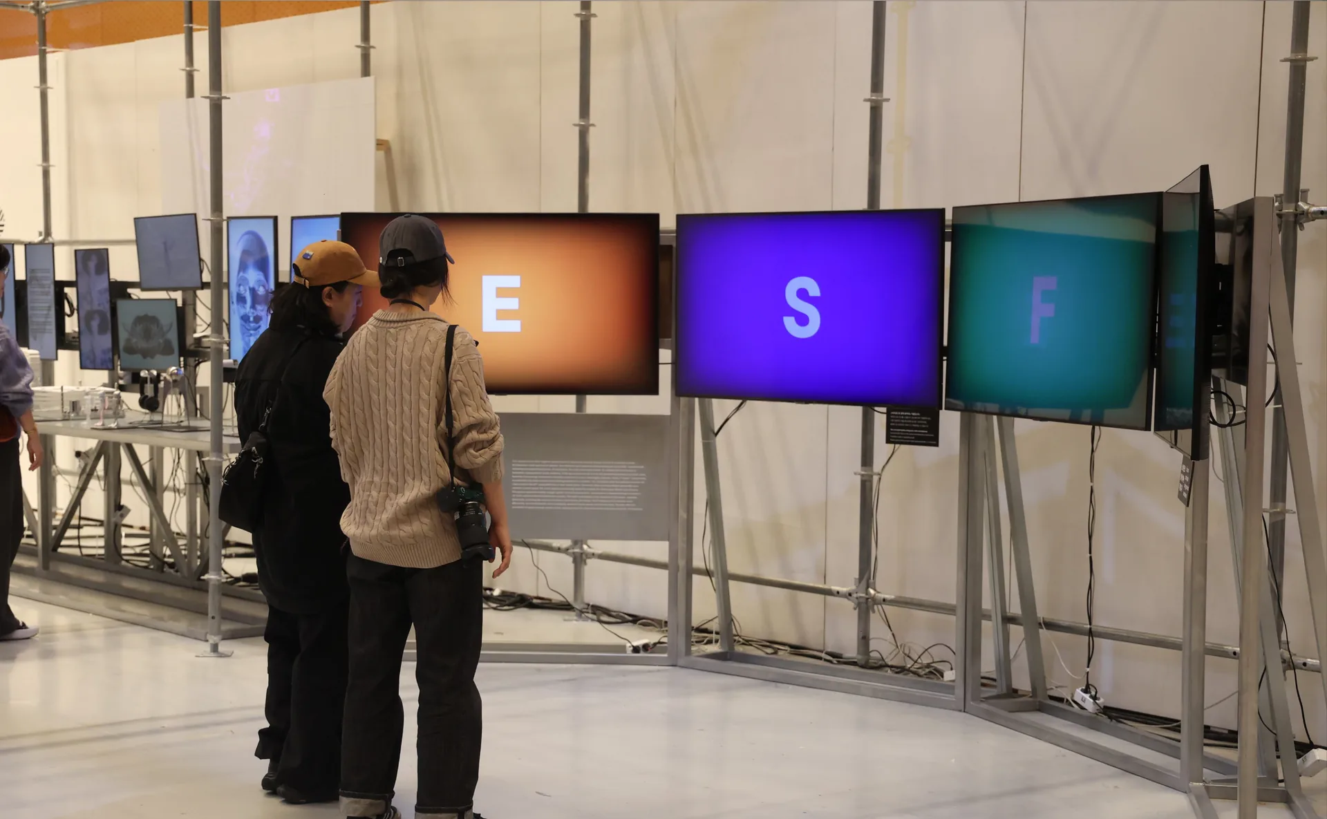 Visitors facing the Ω installation as the screens show coloured letters. Artwork by Jeanyoon Choi.