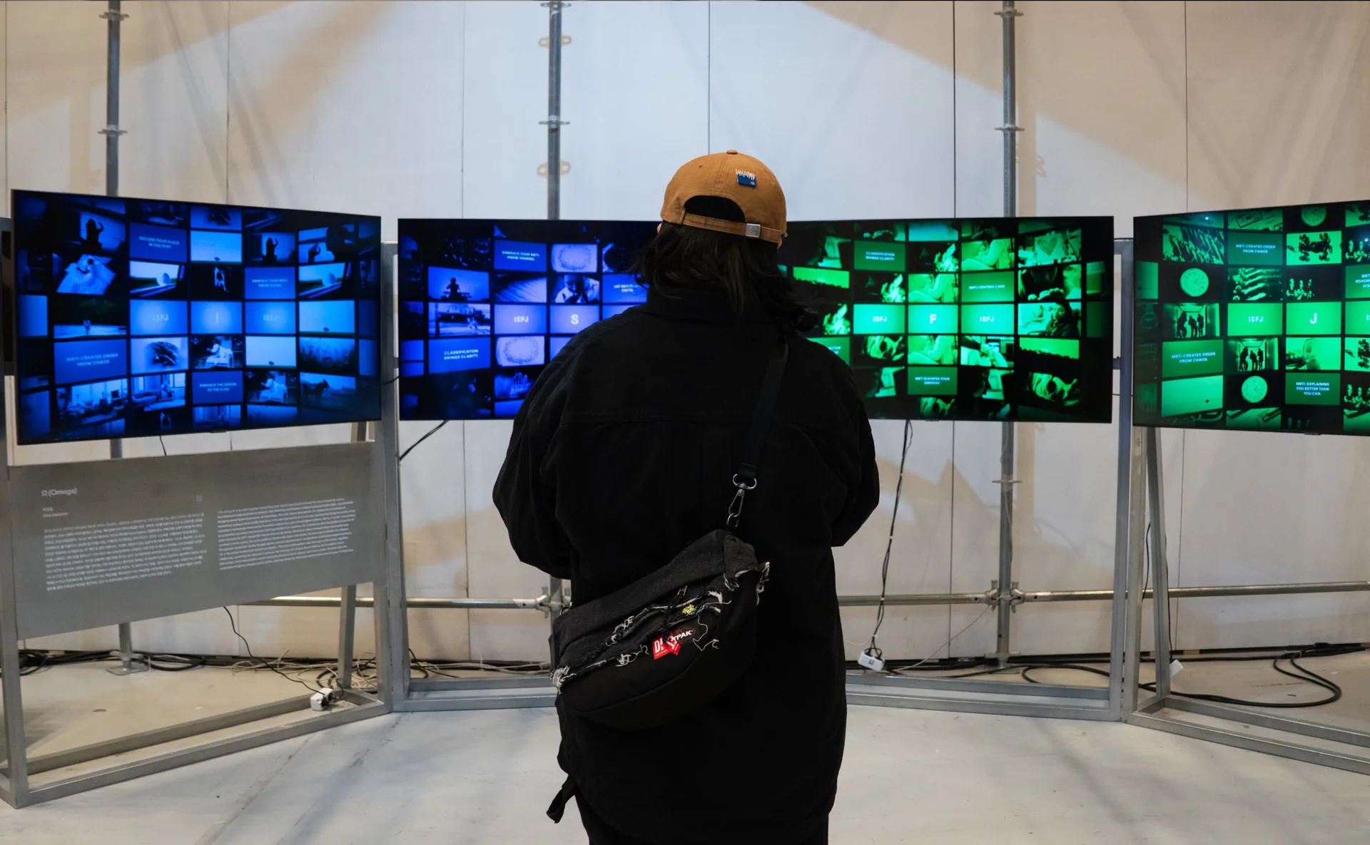 Visitor looking at four Ω screens displaying blue and green image sequences. Artwork by Jeanyoon Choi.